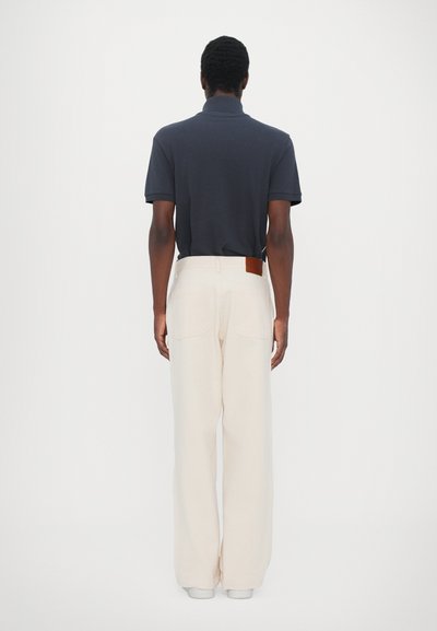 Navy polo shirt with a collared neckline paired with cream wide-leg trousers featuring a brown leather tag on the waistband.