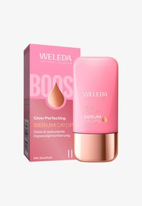 Krople serum Weleda Glow Perfecting w różowej butelce z różowo-złotą podstawą, w towarzystwie dopasowanej różowej pudełka z tekstem i logo.