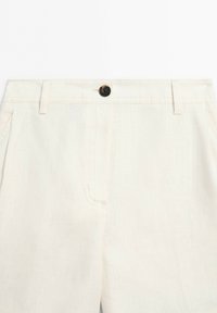 Close-up of beige linen pants waistband with a dark button, belt loops, and front pockets visible.