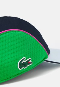 Căciulă cu un corp texturat verde, vizieră bleumarin și accente roz. Prezintă un patch cu logo alb și verde pe lateral.