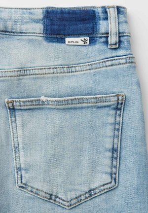 Poche arrière d'un jean en denim bleu clair avec une étiquette de taille 24 et un patch cousu bleu foncé au-dessus de la ceinture.