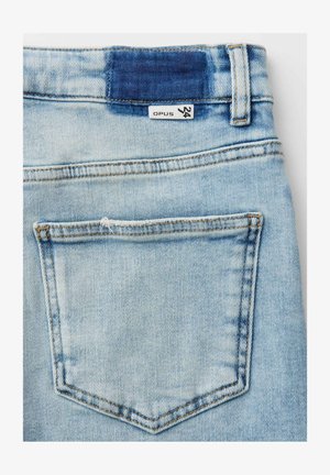 Light blue denim jeans back pocket with a size 24 label and a dark blue stitched patch above the waistband.