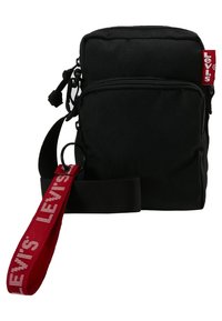 Borsa a tracolla nera in tessuto con tasca frontale con zip, tracolla regolabile e dettaglio della tracolla in rosso con logo. Forma rettangolare compatta.