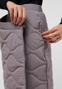 Gequiltede grijze rok met een golvend patroon, voorzien van een zijrits en een elastische tailleband. De stof heeft een zachte, gestructureerde afwerking.