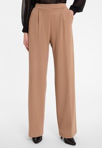 Beige wijde broek met een vlakke voorkant, met plooien, zijzakken en een gladde textuur. Gekocht met zwarte hakken.