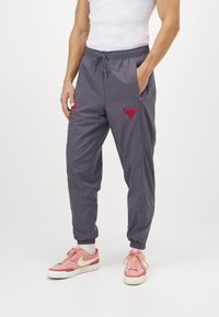 Grå lätta joggingbyxor med elastisk midja, snörning och sidofickor. Har röd broderad Bulls-logotyp och matchande detaljer.