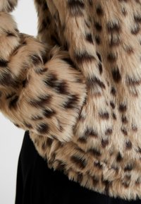 Leopardi-kuosiset tekoturkistakit, joissa on pehmeä, teksturoitu kangas. Ruskean ja beigen sävyjä tummilla pilkuilla, joissa on ylellinen ja volyymikas muotoilu.