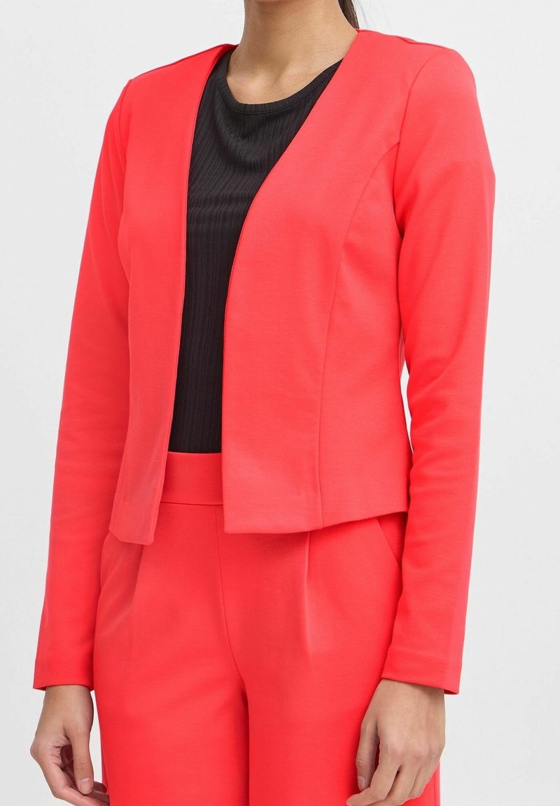 Korallfärgad blazer av slät tyg, med öppen front, långa ärmar och en figurnära silhuett, kombinerad med en svart topp under.