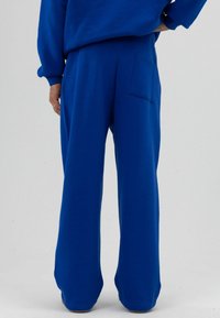 Blauwe, wijde sweatpants gemaakt van een zachte stof; voorzien van een achterzak en een ontspannen pasvorm. Gestructureerd oppervlak zonder zichtbare patronen.