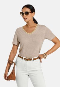 Beiges V-Ausschnitt-T-Shirt mit einem hellgelben Saum, kombiniert mit weißen Jeans, einem braunen Gürtel und einer braunen Handtasche, accessorisiert mit Sonnenbrillen.
