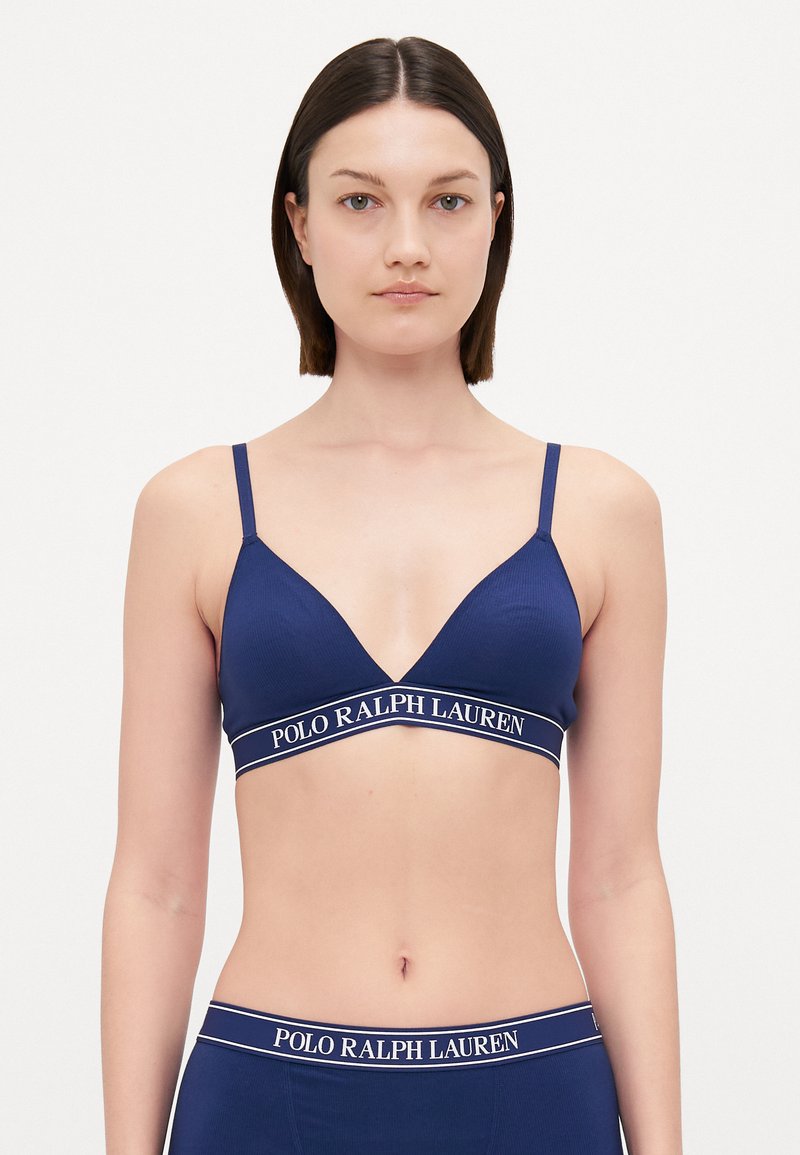 Mörkblå triangelformad bralette med tunna band, med en texturerad tyg och en kontrasterande vit logoband under bysten.