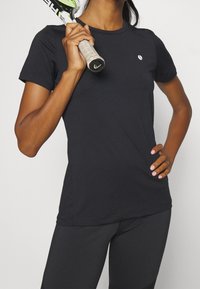 Camiseta deportiva negra de manga corta, ajuste slim, con cuello redondo, hecha de tela suave, diseño minimalista, con un pequeño logo en el pecho.