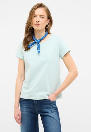 Camiseta de algodón azul clara de manga corta, con cuello redondo y un pequeño logotipo de velero blanco. Combinada con jeans de color azul oscuro y una bufanda azul con estampado.