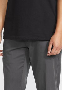 Black cotton t-shirt paired with gray trousers, featuring a smooth texture and a straight cut. The t-shirt has short sleeves and a crew neck.