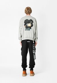Sudadera gris con un diseño de dibujos animados en la parte trasera, combinada con pantalones cargo negros que tienen bolsillos laterales y una correa con patrón, y botas marrones.