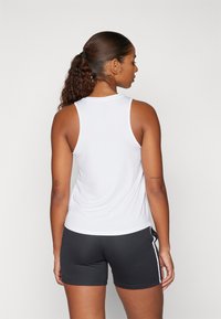 Hvit atletisk tank topp med rund hals og ermeløs design, kombinert med svarte shorts med hvite sidestriper og en glatt tekstur.