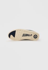 Black sneaker sole with textured rubber for grip; features a beige outsole and printed logo in the heel area. Hexagonal tread pattern.