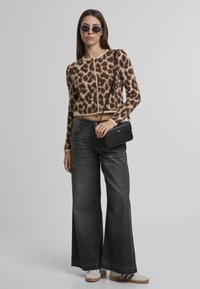 Hnedý a béžový leopardí vzor cropped kardigán, doplnený o široké tmavosivé džínsy a čiernu kabelku cez rameno. Okuliare na slnko dopĺňajú vzhľad.