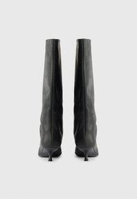 Fekete bőr, térd fölé érő csizmák, testhez simuló dizájnnal, hegyes orral és kicsi stiletto sarkakkal. Sima felület, enyhe ráncokkal.