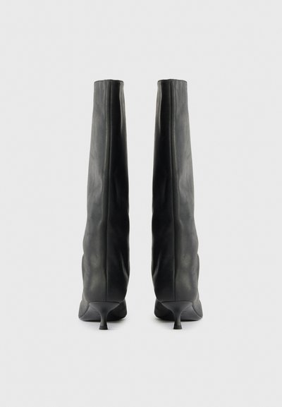 Bottes en cuir noir montantes, avec un design ajusté, des bouts pointus et de petits talons aiguilles. Texture lisse avec des plis subtils.
