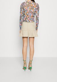 Långärmad blommig bodysuit med svart bakgrund, parat med en beige volangmini kjol och gröna sandaler med remmar.