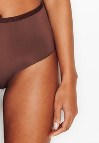 Sous-vêtements marron taille haute en tissu lisse avec une taille élastiquée, présentant un design sans coutures et une coupe ajustée.