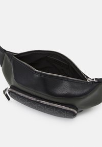 Musta nahkavyölaukku, jossa on avoin päävetoketjupalvelu ja etuvetoketjupuoli, jossa on toistuva logomalli.