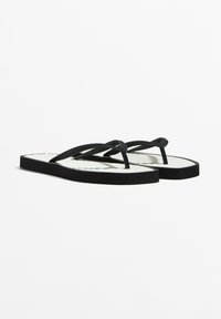 Zwarte flip-flops met dunne banden, voorzien van een gestructureerde witte voetbed en een platte zwarte zool. Strak, minimalistisch ontwerp geschikt voor casual gebruik.