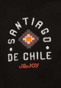 Zwarte stof met witte en oranje geborduurde tekst: "Santiago de Chile" met een geometrisch ontwerp in grijze en oranje accenten.