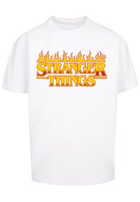 Weißes Baumwoll-T-Shirt mit fettem, orangefarbenem "STRANGER THINGS"-Text und stilisierten Flammenakzenten oben. Kurze Ärmel und lockere Passform.