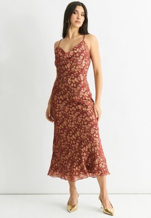 Red sleeveless dress with a cowl neckline, featuring a gold leopard print pattern. Flowing fabric and a midi length, with a scalloped hem.