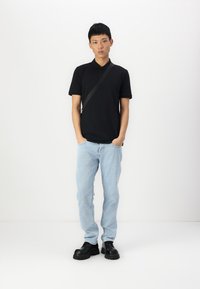 Camisa polo preta de manga curta, jeans claros de perna reta e sapatos de salto preto, usados com uma bolsa transversal preta. Design simples.