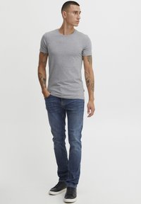 Tricou gri cu guler rotund, fabricat din bumbac, asortat cu blugi negri din denim. Blugii au o croială slim și modelul poartă pantofi sport negri.