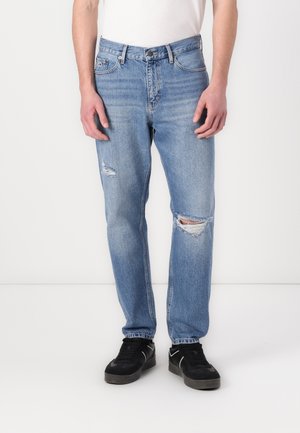 Lyseblå denimjeans med avslappet passform, som har slitte detaljer og to hull ved knærne, kombinert med svarte joggesko.