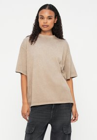 Overdimensioneret, kortærmet beige t-shirt med rund hals og blødt, tekstureret stof. Kombineret med mørke cargo-bukser, der har lommer.