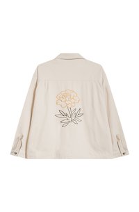 Veste en chemise beige à manches longues, avec une broderie florale au dos en orange et noir. Fabriquée en tissu texturé avec des accents de boutons.