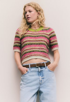 Kortärmad, kort tröja med färgglada ränder i rosa, grönt och svart, tillverkad av ett strukturerat stickat material. Bärs med ljusblå jeans.