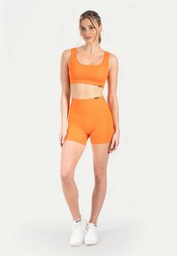 Oranges Sportoutfit bestehend aus einem kurzen Oberteil und hoch taillierten Shorts. Hergestellt aus dehnbarem Material mit glatter Textur und minimalem Branding.