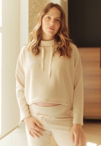 Lichtbeige, geribbelde brei lounge-outfit bestaande uit een cropped pullover met een hoge hals en koordjes, gecombineerd met broek met elastische tailleband.