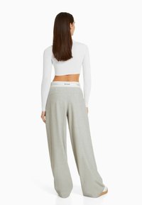 Light gray wide-leg trousers with a smooth texture, featuring back pockets and an elastic waistband labeled "TOO CLOSE." Styled with a white cropped top.