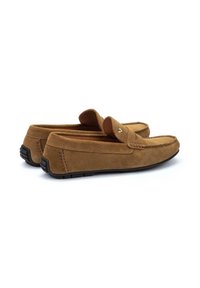 Mocasines de ante marrón con suela plana de goma negra, que presentan detalles de costura y un sutil diseño elevado en el empeine.
