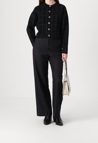 Cardigan corto nero con motivo a scacchi e bottoni argentati, abbinato a pantaloni neri a vita alta e una borsa leggera. Stivaletti neri.