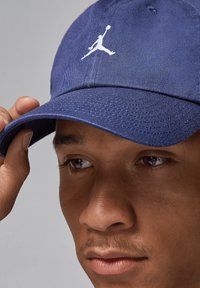 Mørkeblå baseball cap laget av strukturert stoff, med et hvitt Jumpman-logo på fremsiden og en buet skjerm.
