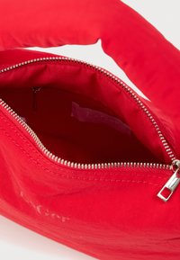 Κόκκινη υφασμάτινη τσάντα χειρός με ασημένιο φερμουάρ εν μέρει ανοιχτό, που δείχνει το εσωτερικό με κόκκινη επένδυση και μια ραμμένη ετικέτα.