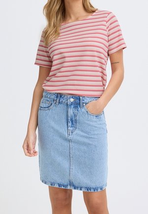 Femme portant un haut à manches courtes rayé rose et blanc, rentré dans une jupe en jean bleu clair jusqu'aux genoux, avec une main dans la poche.