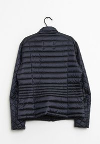 Svart vadderad pufferjacka hängande på en svart galge mot en vit bakgrund, visad från baksidan.