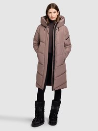 Gewatteerde lange jas in lichtbruin, met trekkoord aan de capuchon, ritssluiting aan de voorkant, zijzakken, gecombineerd met zwarte sneeuwlaarzen.