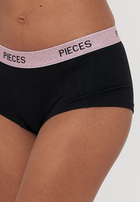 Černé hipsterské spodní prádlo s lesklým růžově zlatým elastickým pasem s nápisem "PIECES". Hladký povrch a přiléhavý design.