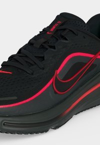 Μαύρο sneaker Nike Air Max με κόκκινες λεπτομέρειες, ορατή αερόσολα, πλέγμα στο άνω μέρος και κείμενο «WINFLO 12» στη γλώσσα της γλώσσας.