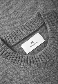 Pulover gri din tricot, cu un finisaj texturat, având un guler ribat și un eticheta albă cu marca "Matinique" aproape de guler.